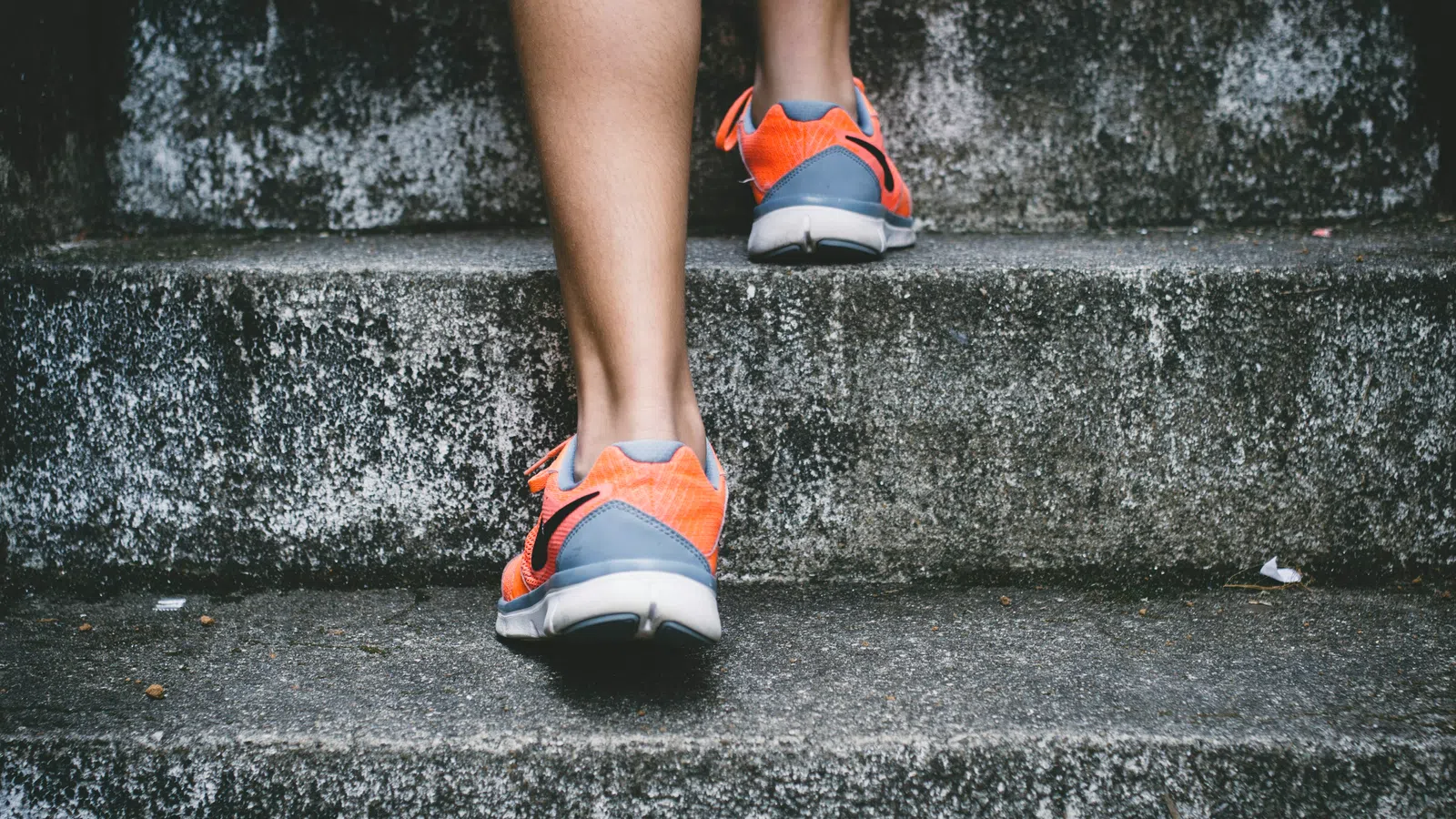 Person wearing orange athletic shoes walking up concrete stairs during exercise or training.