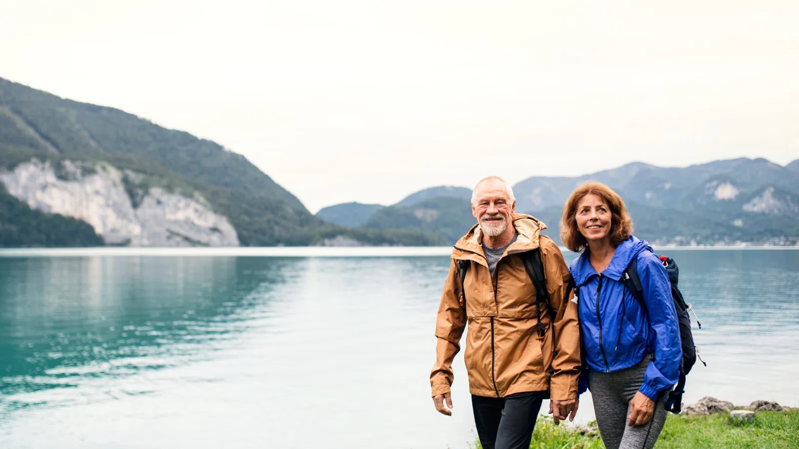 a man and woman standing by a body of water with mountains in the background