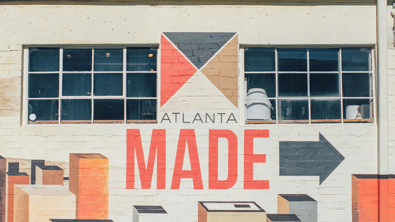 Mural on a building with geometric shapes and text 'ATLANTA MADE' under two windows against a clear sky.