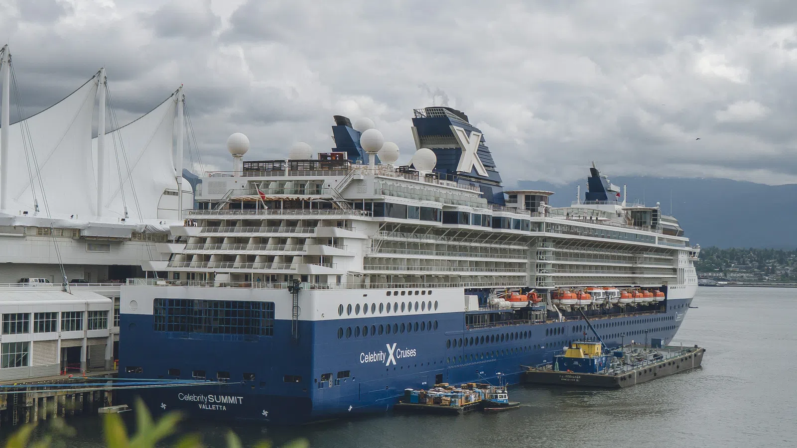 Celebrity Summit cruise ship docked at a port with cloudy sky and green foliage in foreground