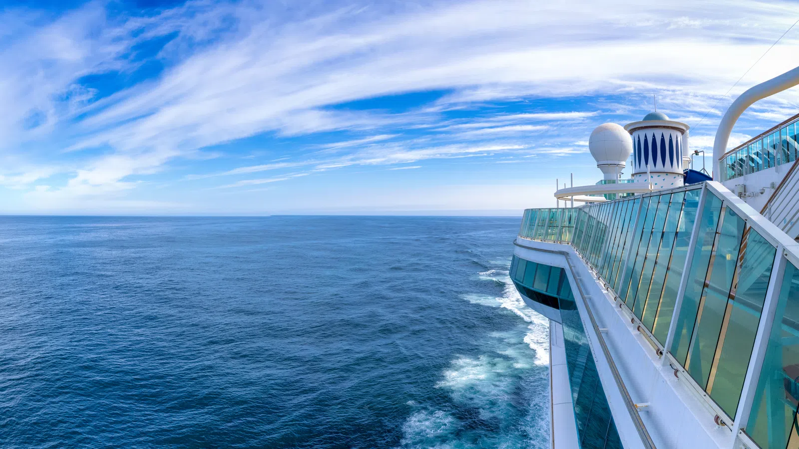 View from a cruise ship deck overlooking deep blue ocean under a partly cloudy sky on a sunny day.