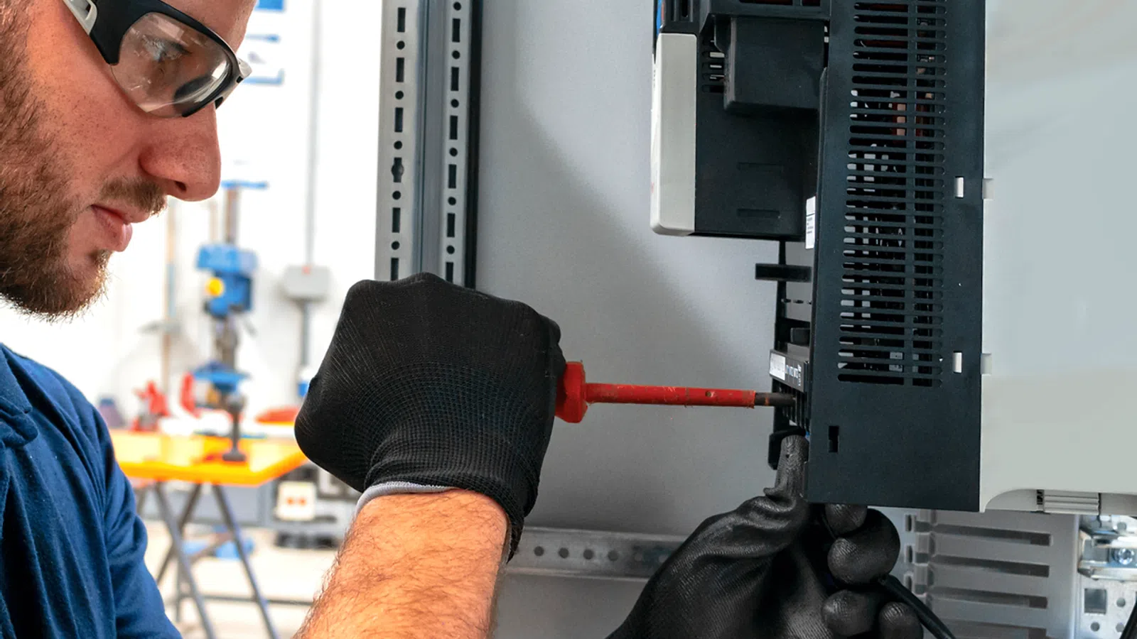 Technician wearing gloves and safety glasses working on electrical control panel with screwdriver