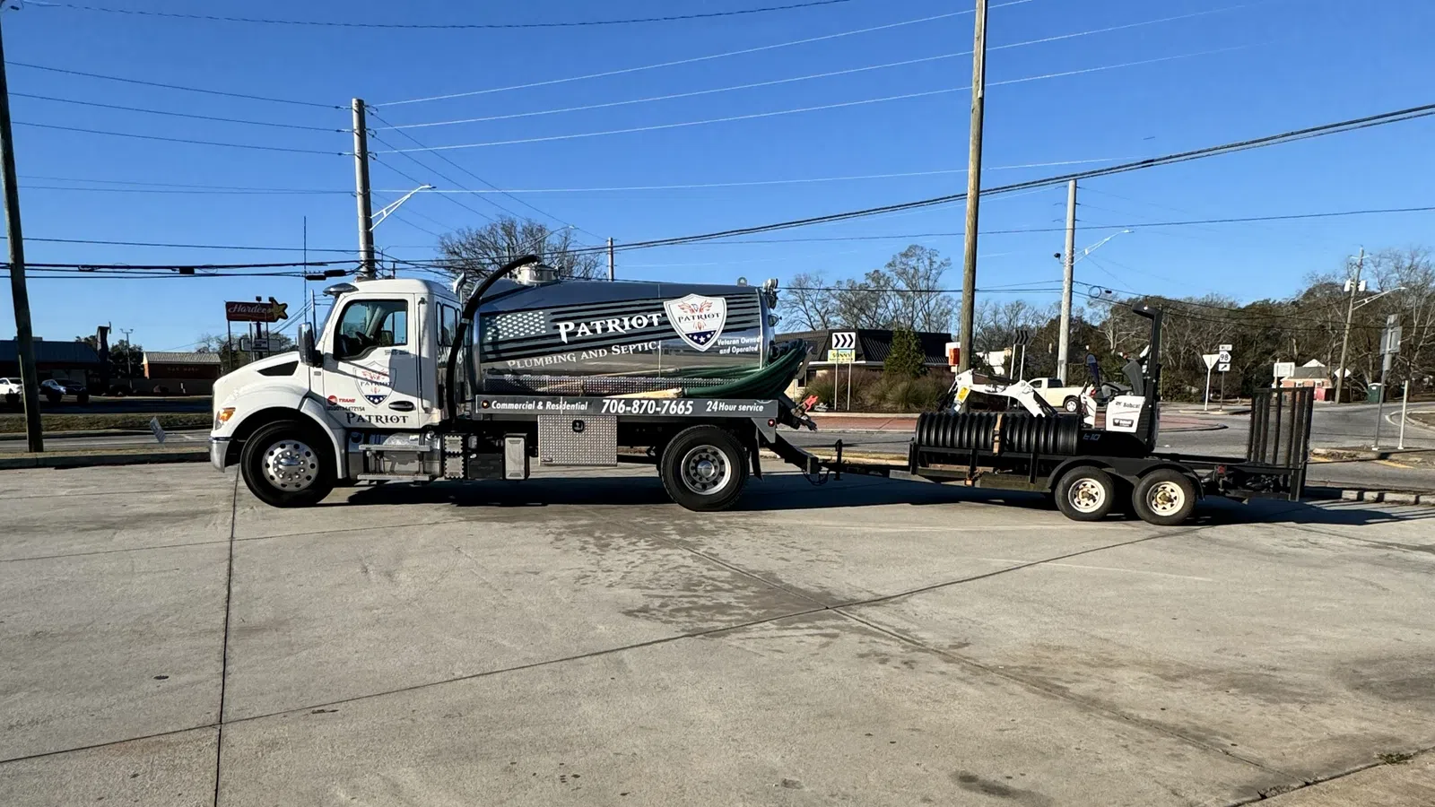 Patriot Plumbing and Septic service truck with equipment trailer parked on a concrete lot under clear sky.