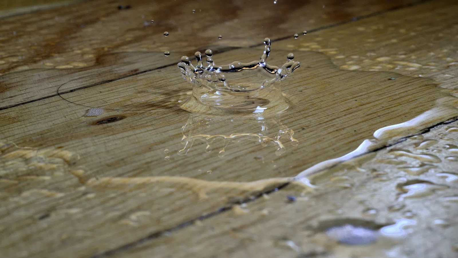Water droplet splash creating a crown shape on a wet wooden surface with reflections and ripples.