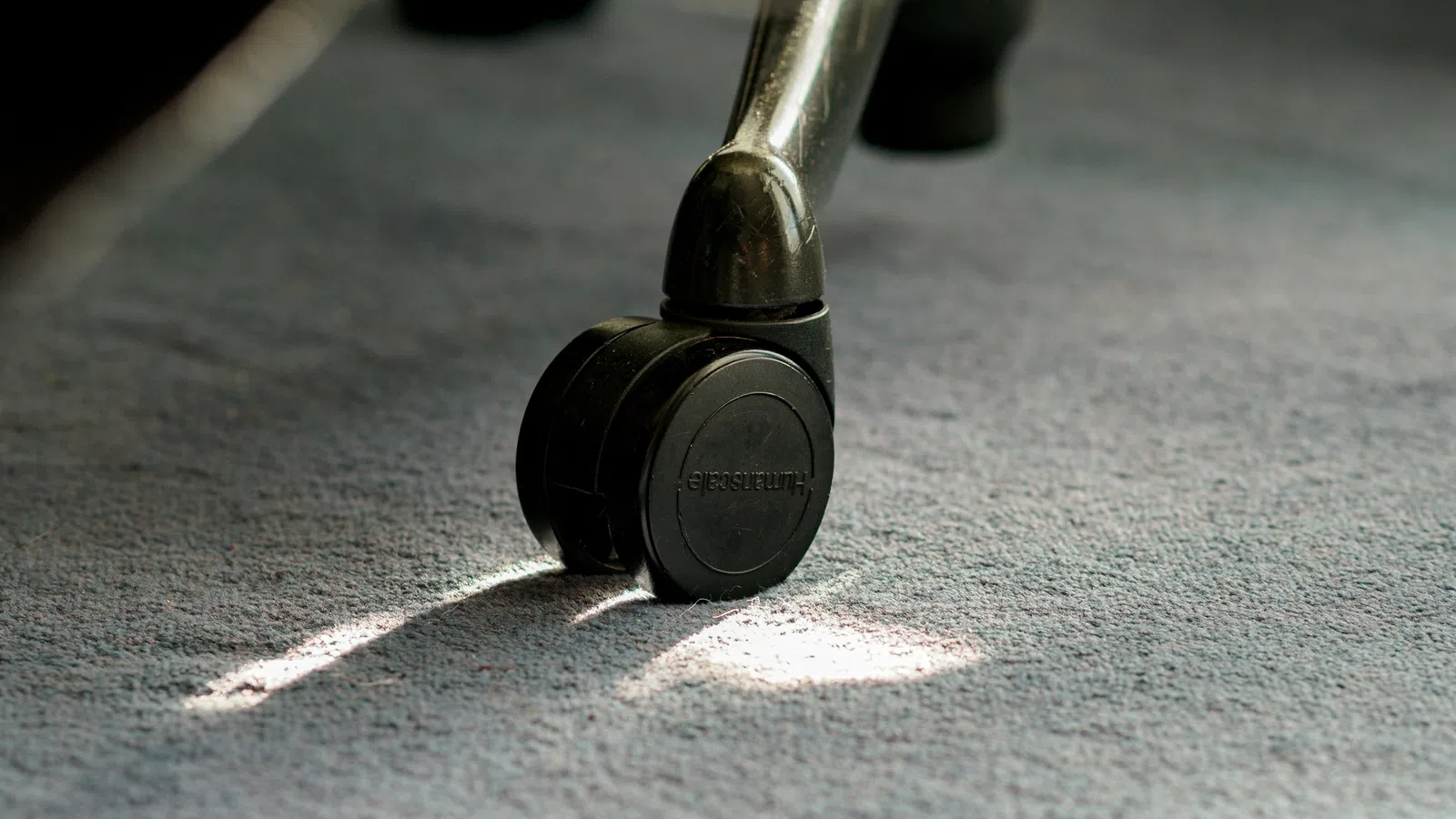 Close-up of a black office chair wheel on a carpeted floor with sunlight casting shadows