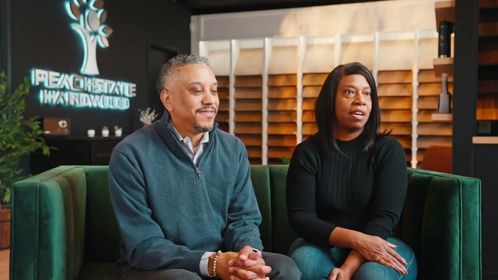 Two people seated on a green couch inside a peach state hardwood showroom with flooring samples in background.