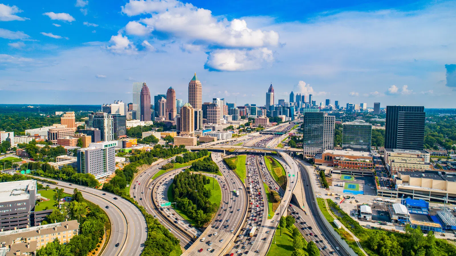 Aerial view of a bustling city skyline with multiple highways merging and traffic under a blue sky with clouds.