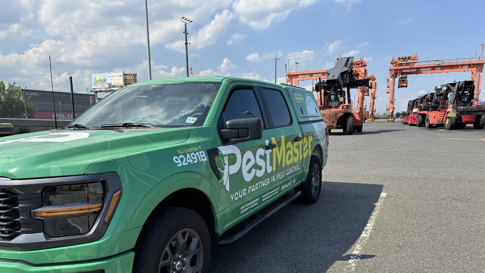 Green PestMaster truck parked in industrial area with cranes and blue sky in the background
