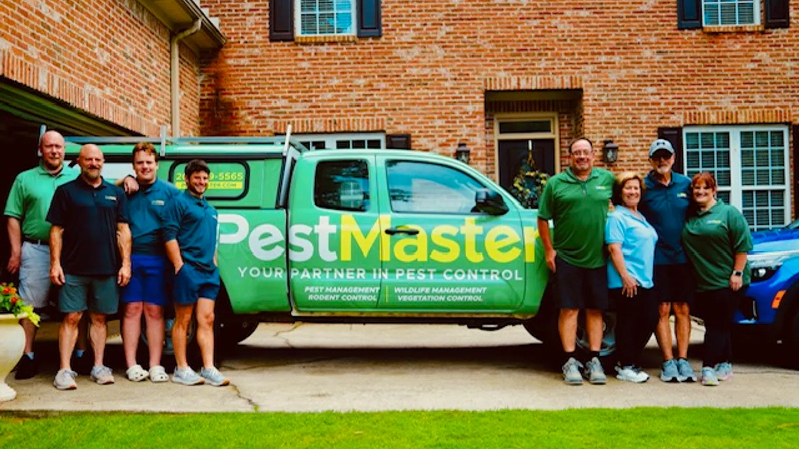 PestMaster pest control team posing beside green company truck, family owned and operated