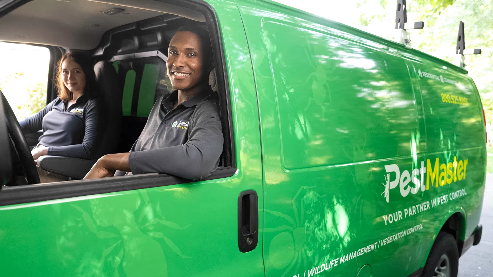 Two PestMaster employees in branded green van ready for pest control services with company logo visible on side.