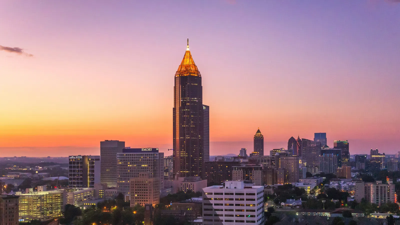 Atlanta skyline at sunset with illuminated Bank of America Plaza tower and vibrant purple and orange sky.