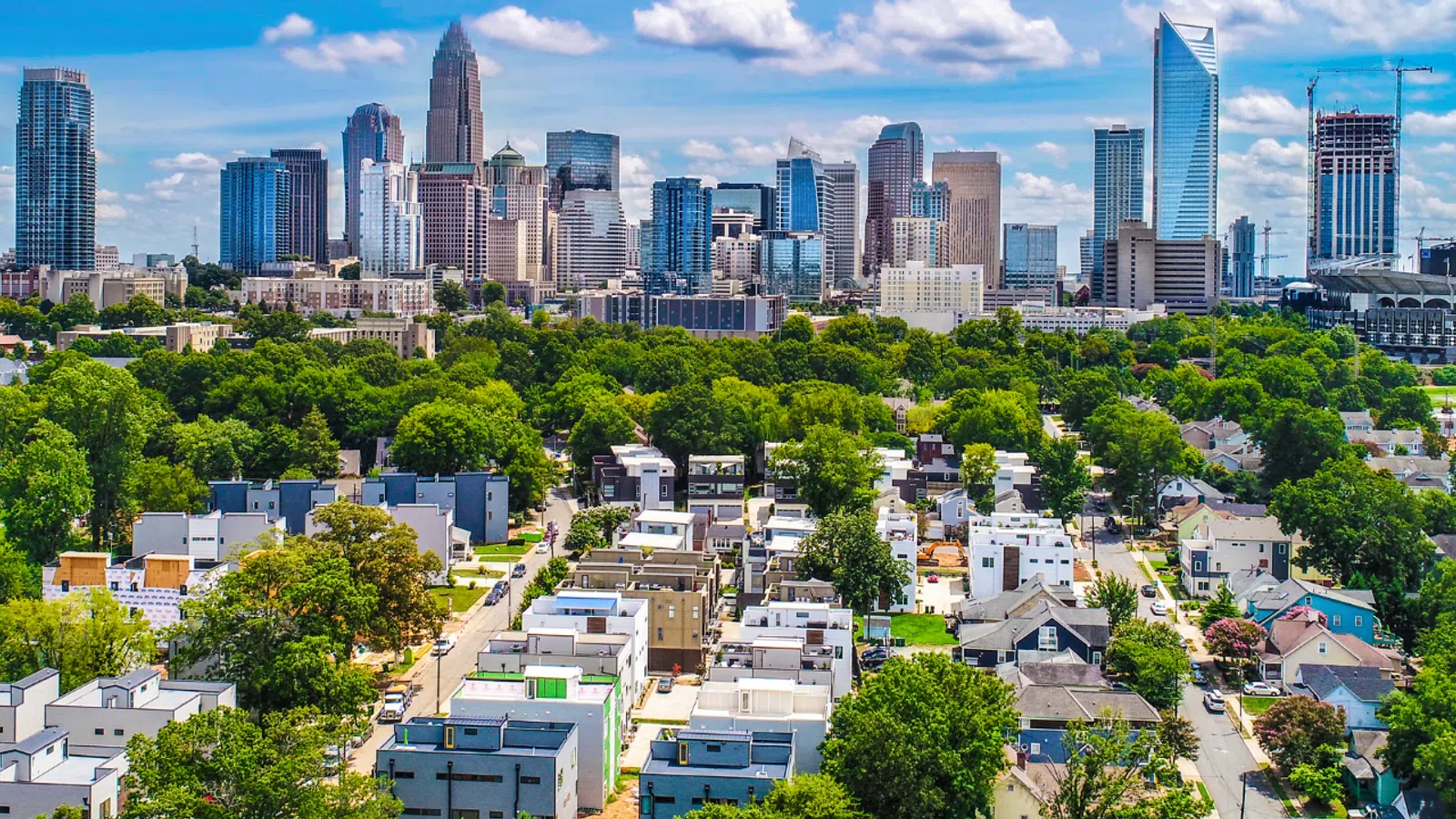 Panoramic view of Charlotte skyline with residential area and lush green trees under blue sky with clouds