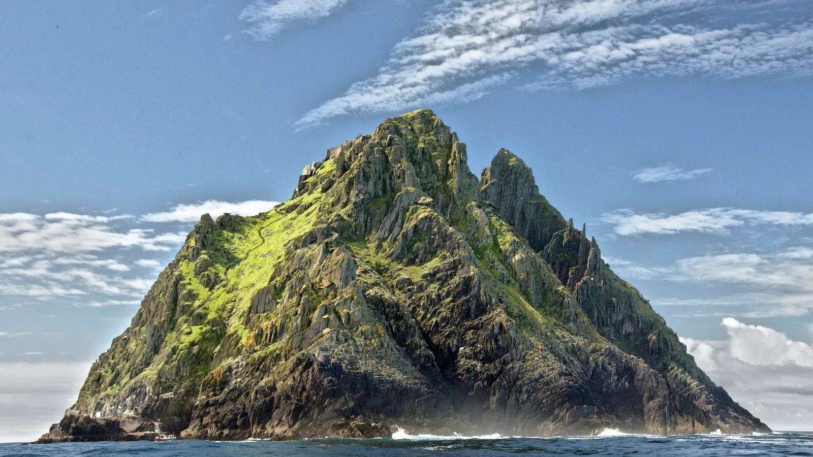 Rocky island with steep cliffs covered in green vegetation surrounded by ocean under partly cloudy sky