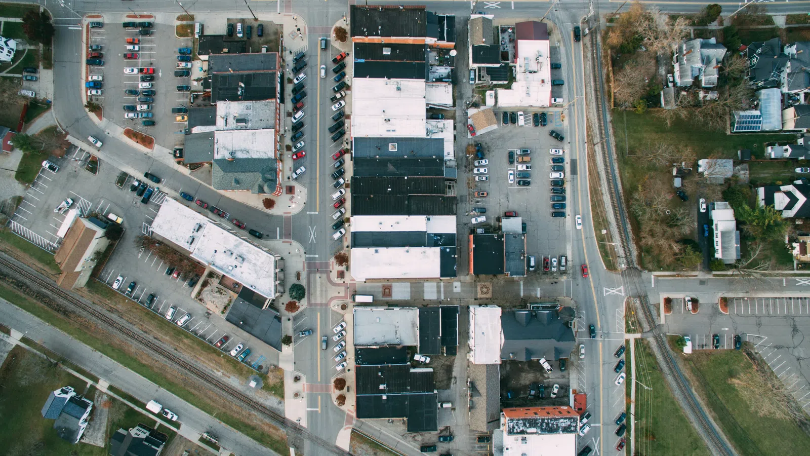 Aerial view of a small town with roads, buildings, parking lots, and train tracks intersecting the area.