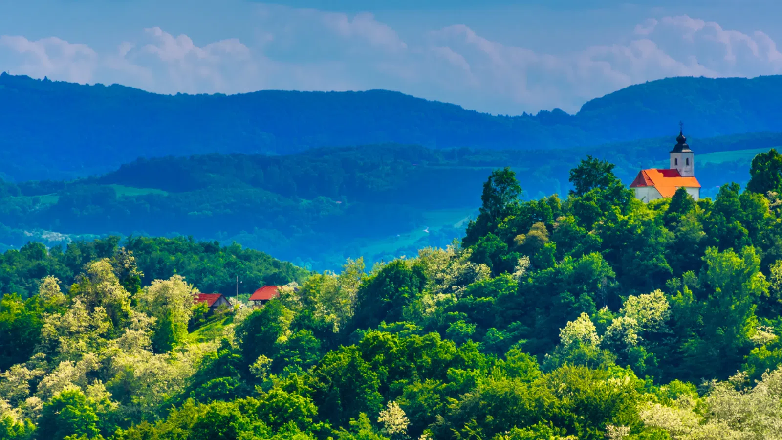 Small church atop a lush green hill with layered blue mountains and sky in the background