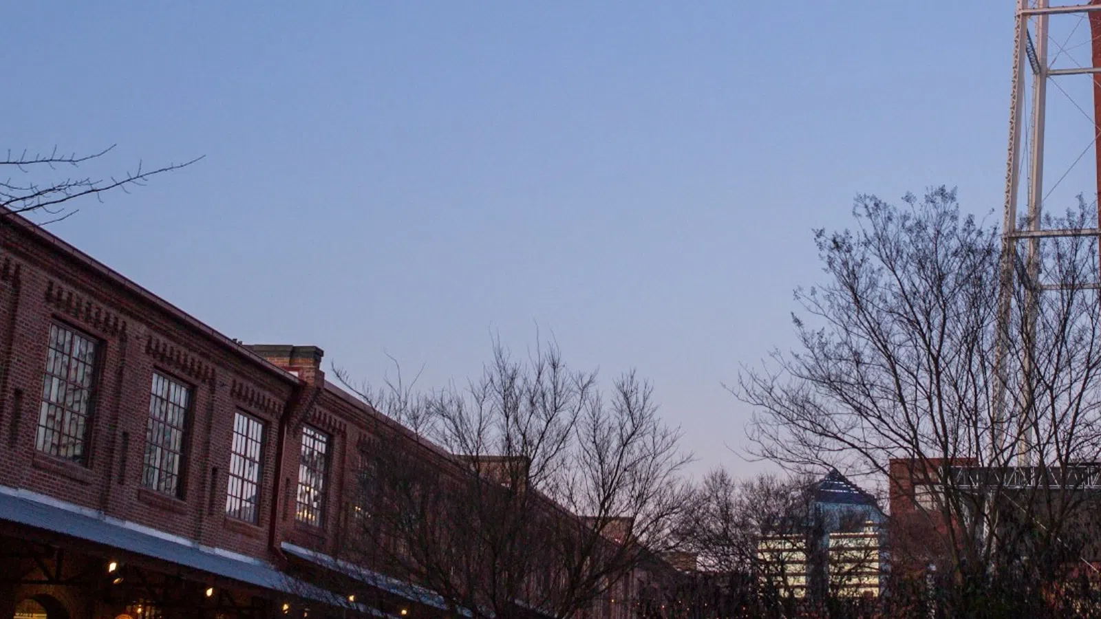 Water tower with Lucky Strike logo towering over historic brick buildings and bare trees at dusk with clear blue sky.