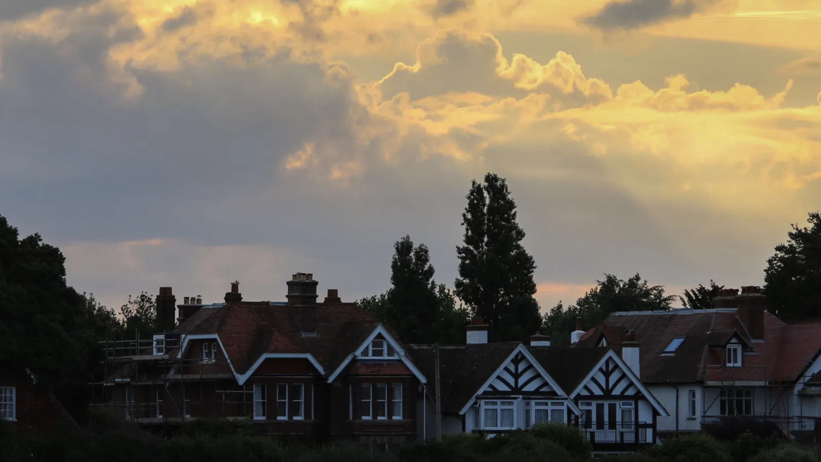 Sunset sky with golden clouds over charming houses and tall trees in a quiet neighborhood.