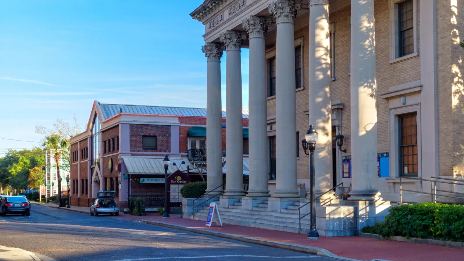 Historic downtown street with classic buildings, columns, parked cars, and clear blue sky on a sunny day