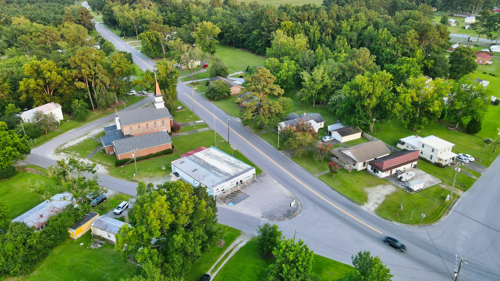 Aerial view of a small rural town with houses, a church, roads, and surrounding green trees and fields