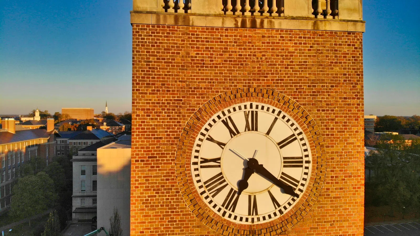 Close-up of a brick clock tower with Roman numerals showing 4:20 against a clear blue sky.