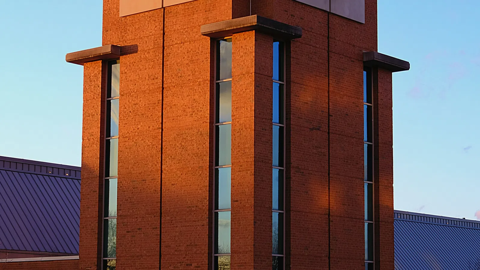 Tall brick clock tower with large clocks on two sides at sunset with clear blue sky background