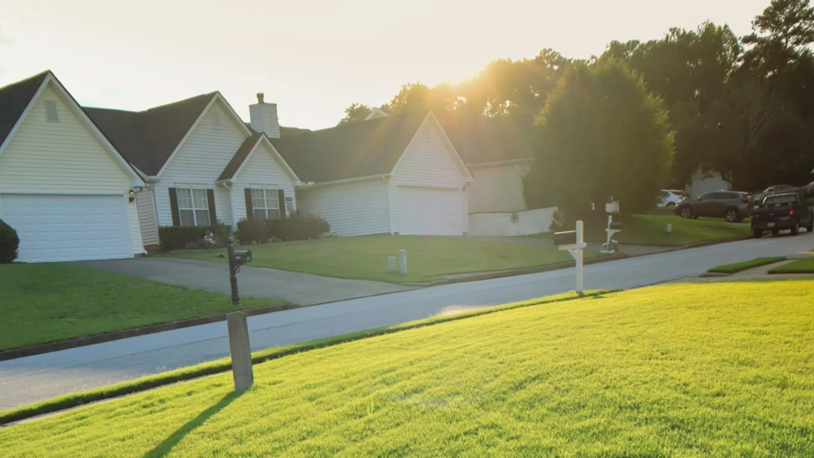 Silver fire hydrant casting a long shadow on green lawn with houses and sunset in the background