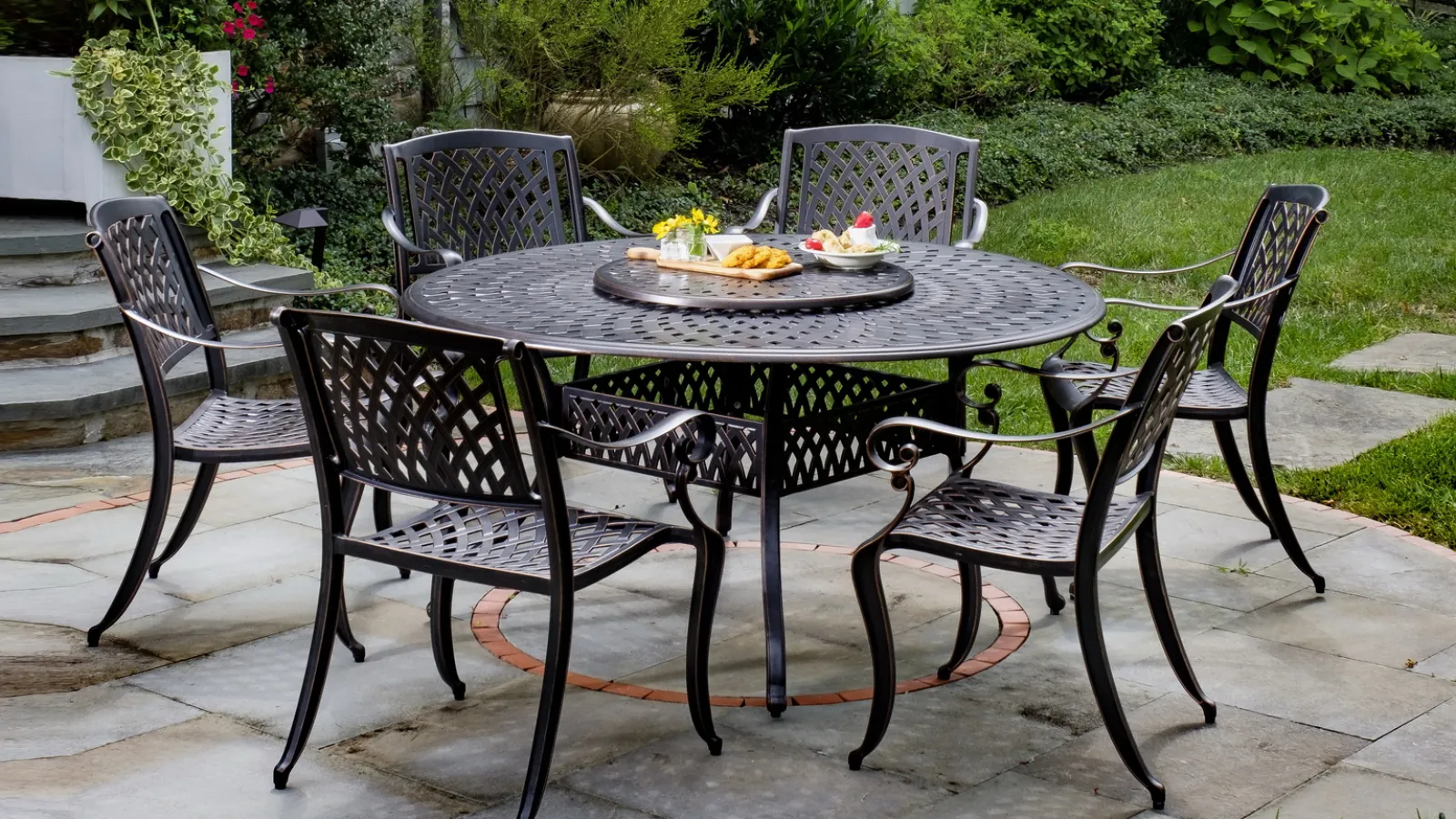 Black metal outdoor dining set with six chairs and snacks on round table in stone patio garden