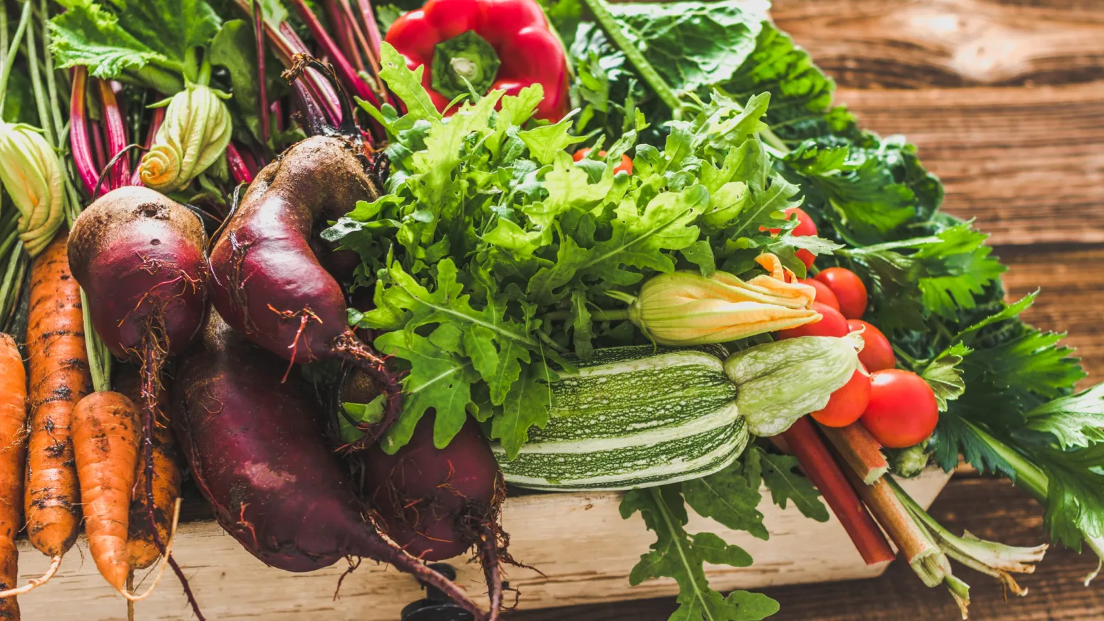 Fresh assortment of organic vegetables including carrots, beets, zucchini, tomatoes, and leafy greens on a wooden table.