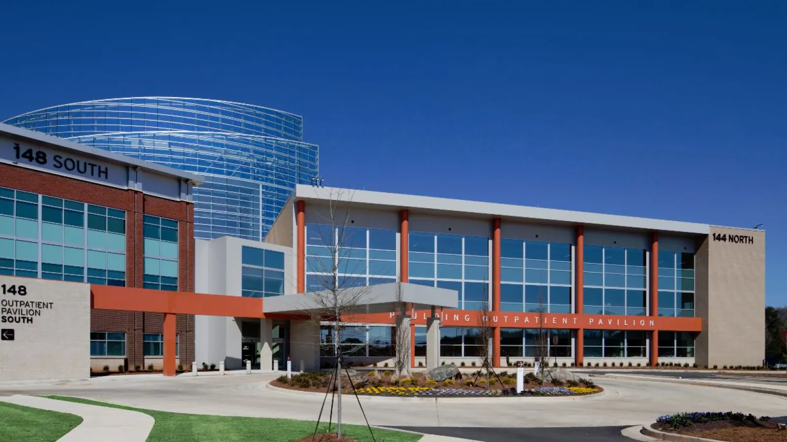 Modern outpatient pavilion with large glass windows and red accents under a clear blue sky.