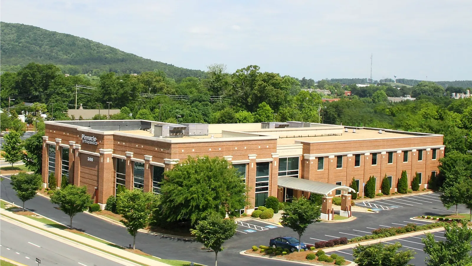 Modern two-story brick commercial building surrounded by trees and parking lot under a partly cloudy sky.