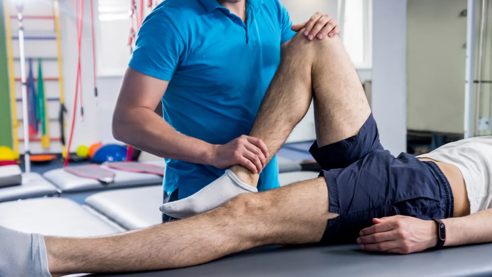 Physical therapist assisting patient with leg stretch in rehabilitation clinic setting.