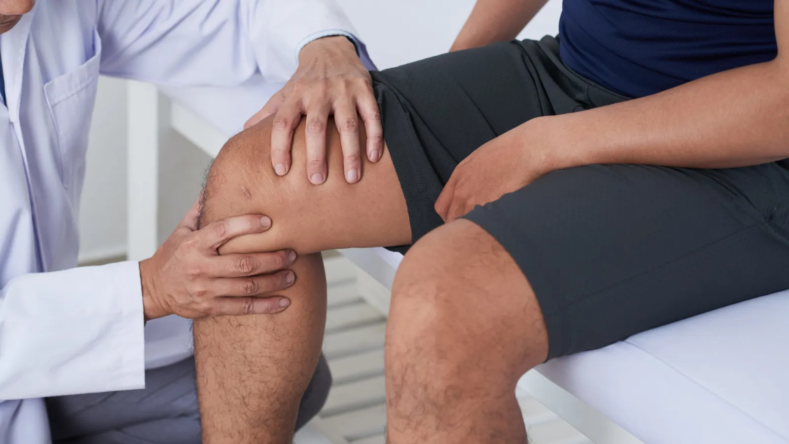 Doctor examining patient's knee joint in a medical consultation for injury or pain assessment.