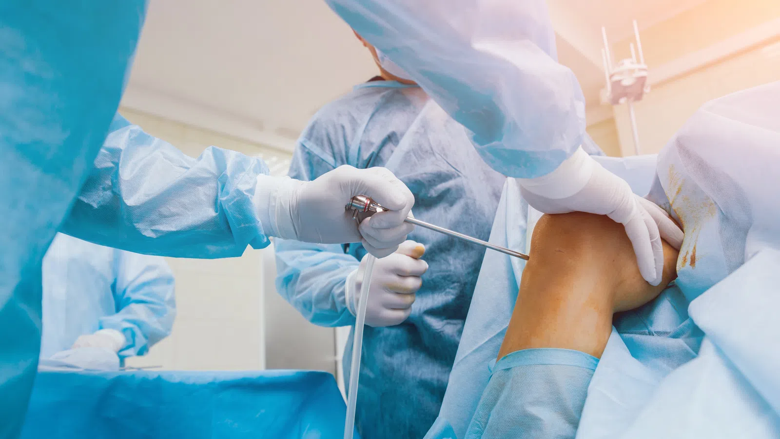 Surgeon performing arthroscopic knee surgery on patient's bent leg in sterile operating room environment