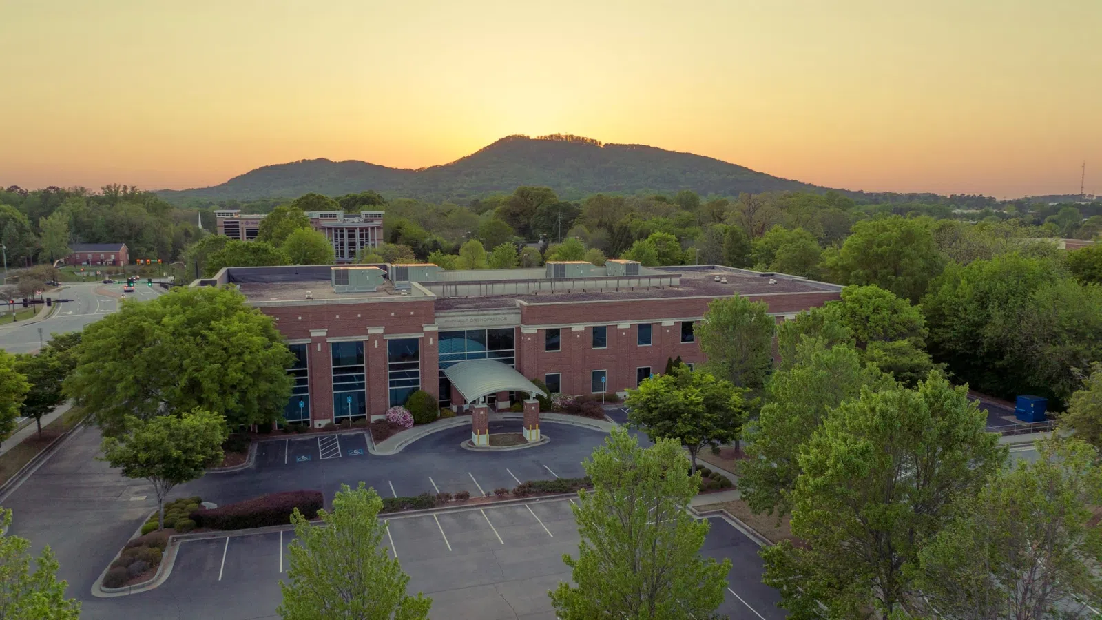 Aerial view of a brick office building with empty parking lot at sunset and hills in the background