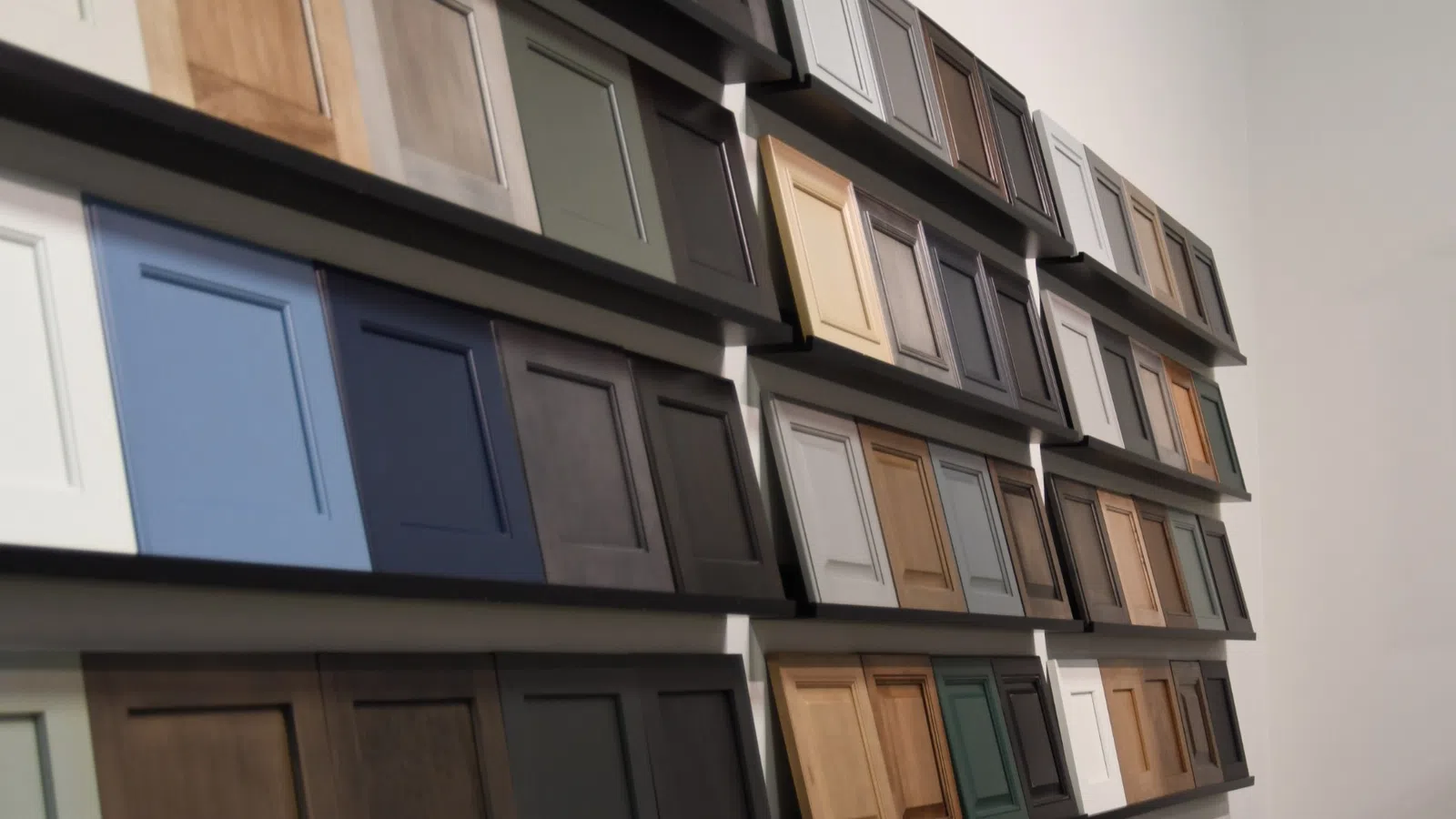 Wall display of various kitchen cabinet door samples in multiple colors and finishes for home remodeling.