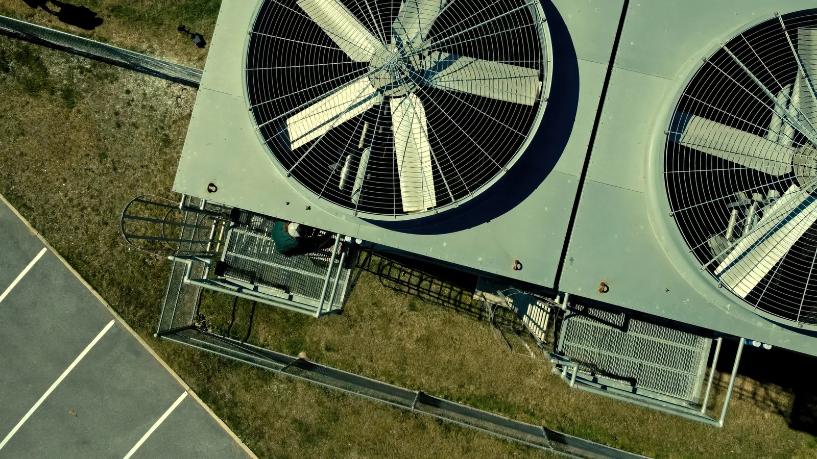 Aerial view of large industrial cooling fans installed on equipment outside near parking and grassy area.