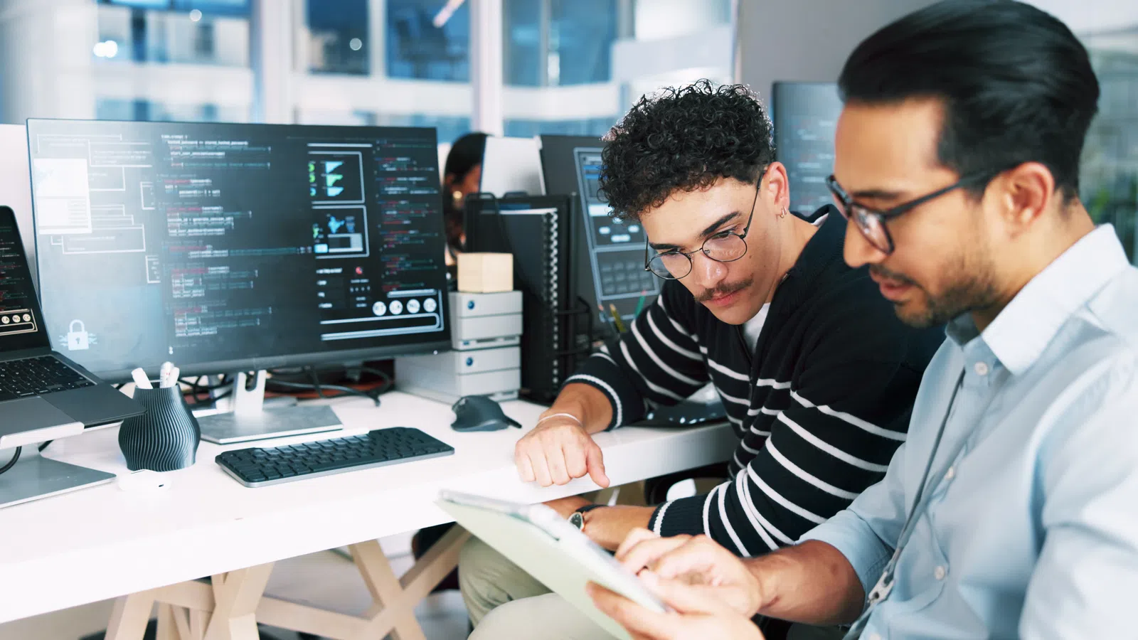 Two software developers collaborating in a modern office with computers displaying code and data visuals.