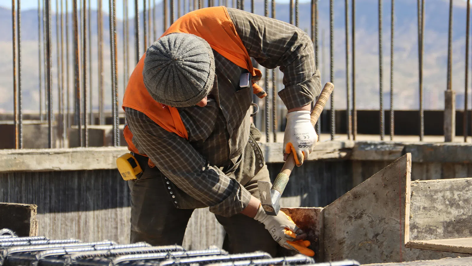 Construction worker wearing safety gear using a tool on concrete structure at a building site.
