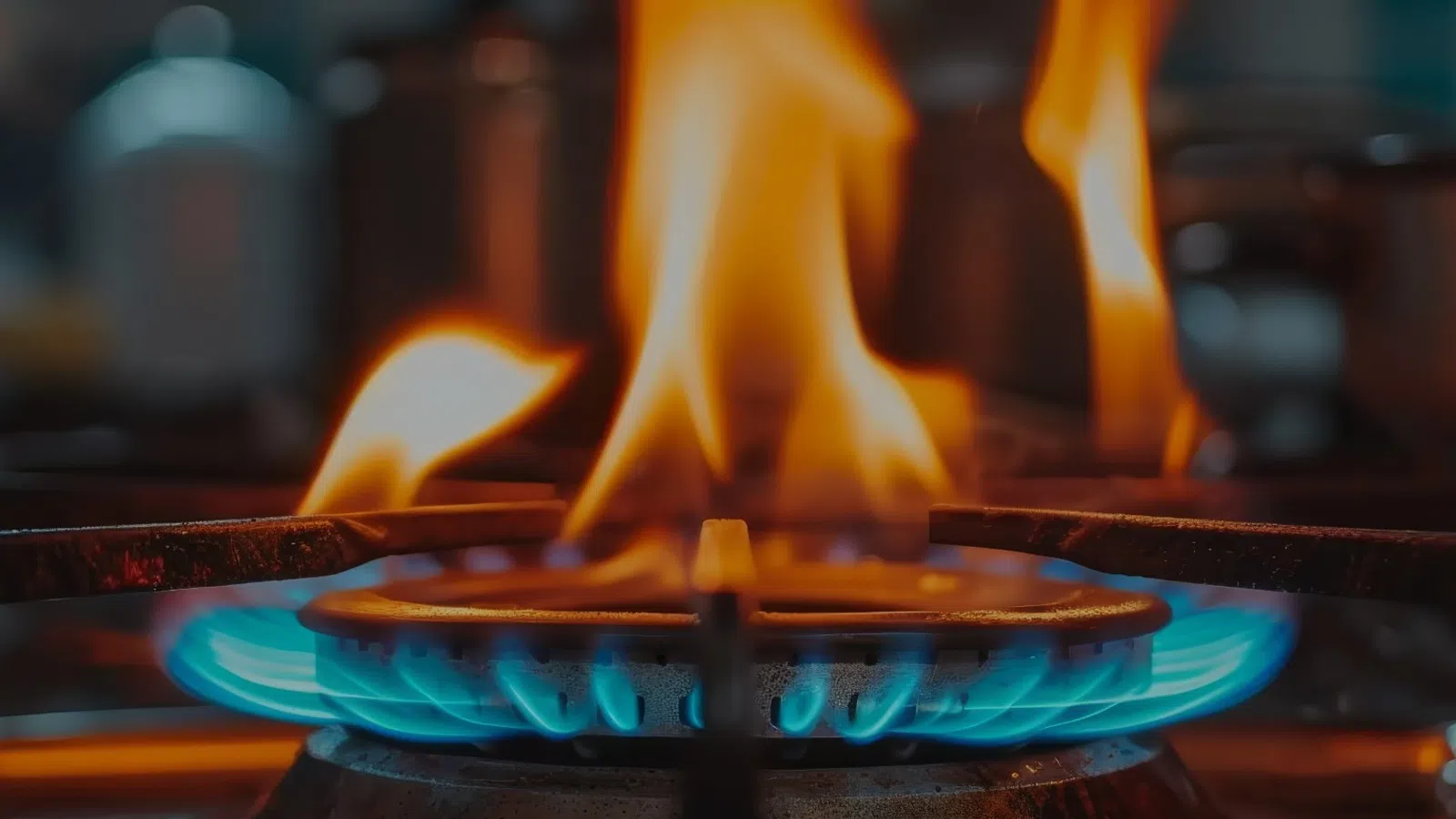 Close-up of a blue gas stove flame with orange fire flames in a kitchen setting.