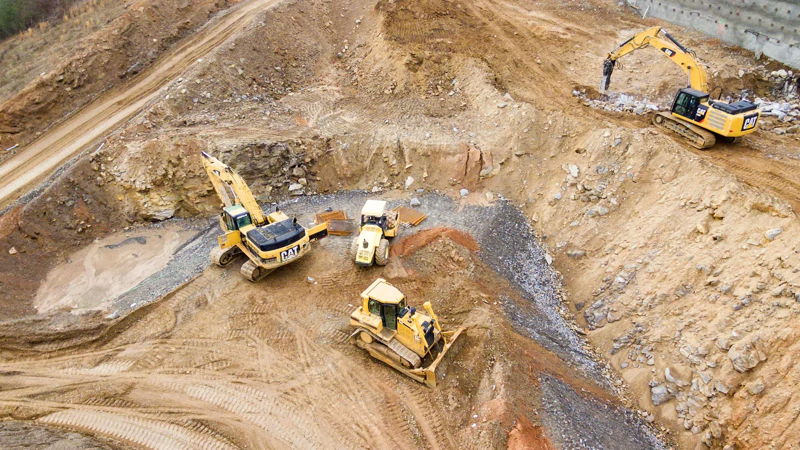 Excavators and bulldozers working in a large open earth excavation site preparing the ground.