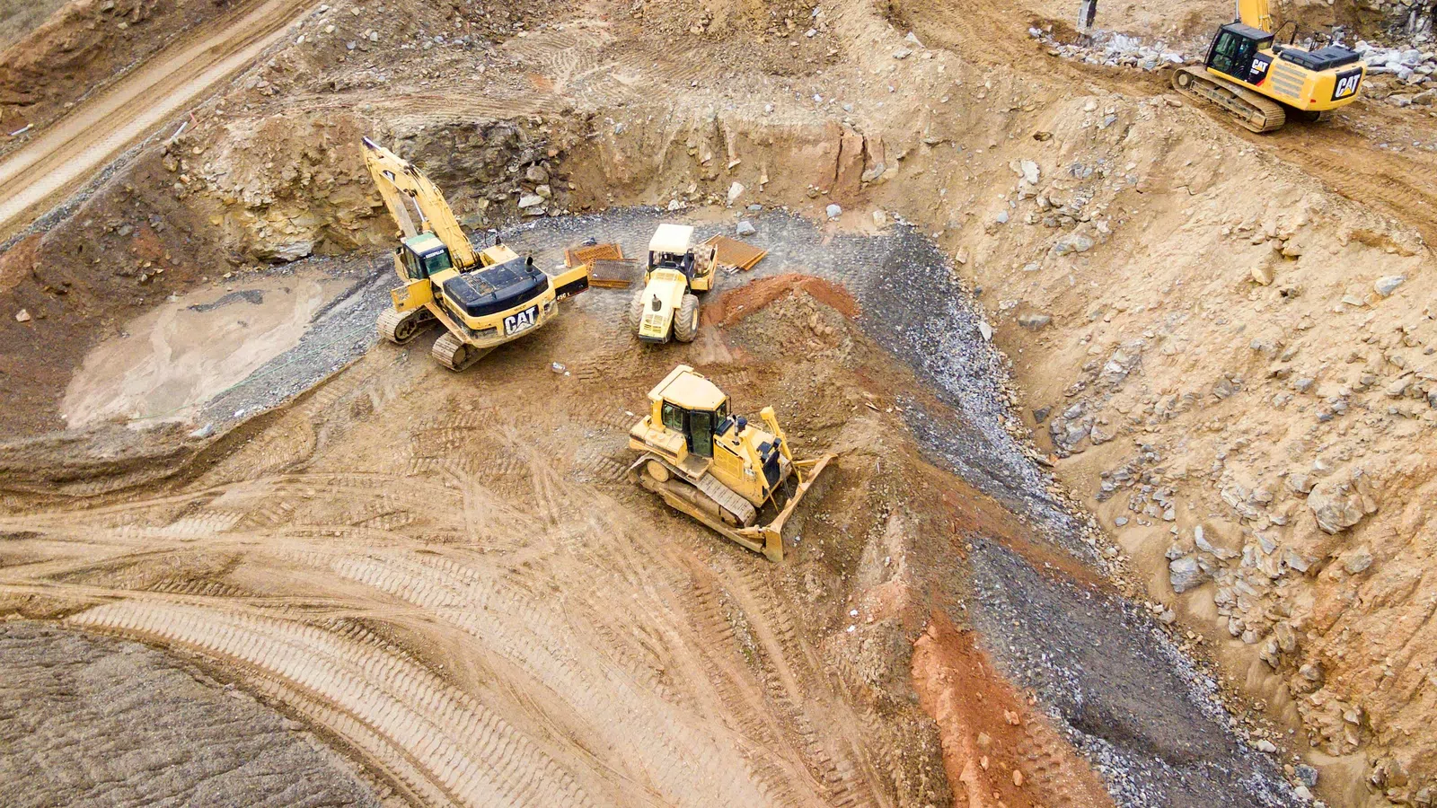 Excavators and bulldozers working in a large open earth excavation site preparing the ground.