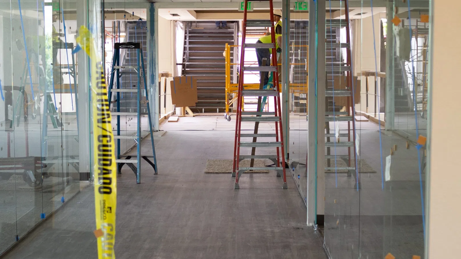 Interior office under construction with ladders, glass walls, and caution tape in a modern building space.