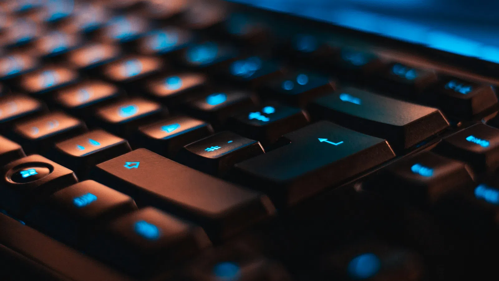 Close-up of a black computer keyboard with blue backlit keys in low light.
