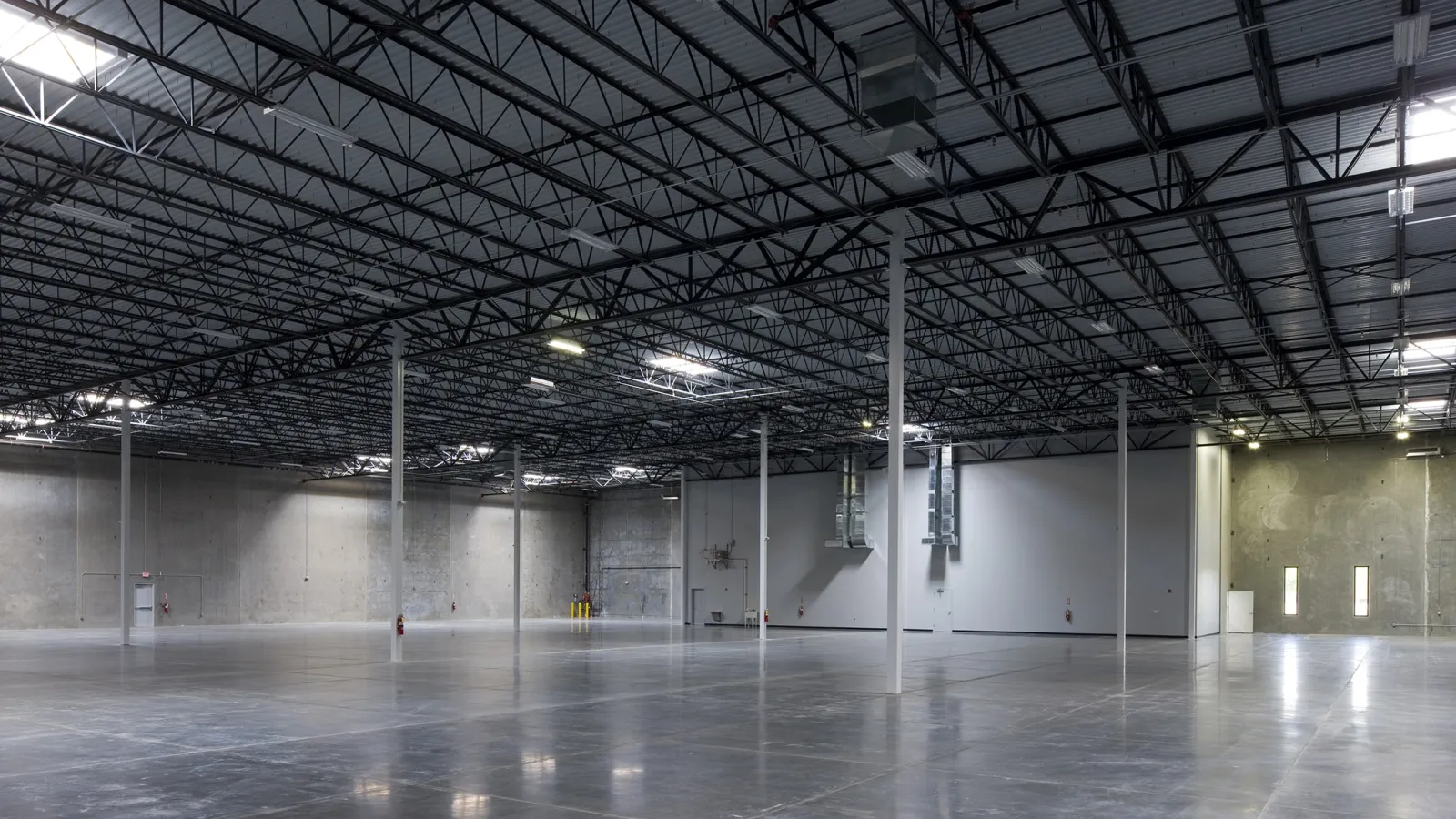 Spacious empty industrial warehouse with polished concrete floor and high ceiling with metal beams and columns.