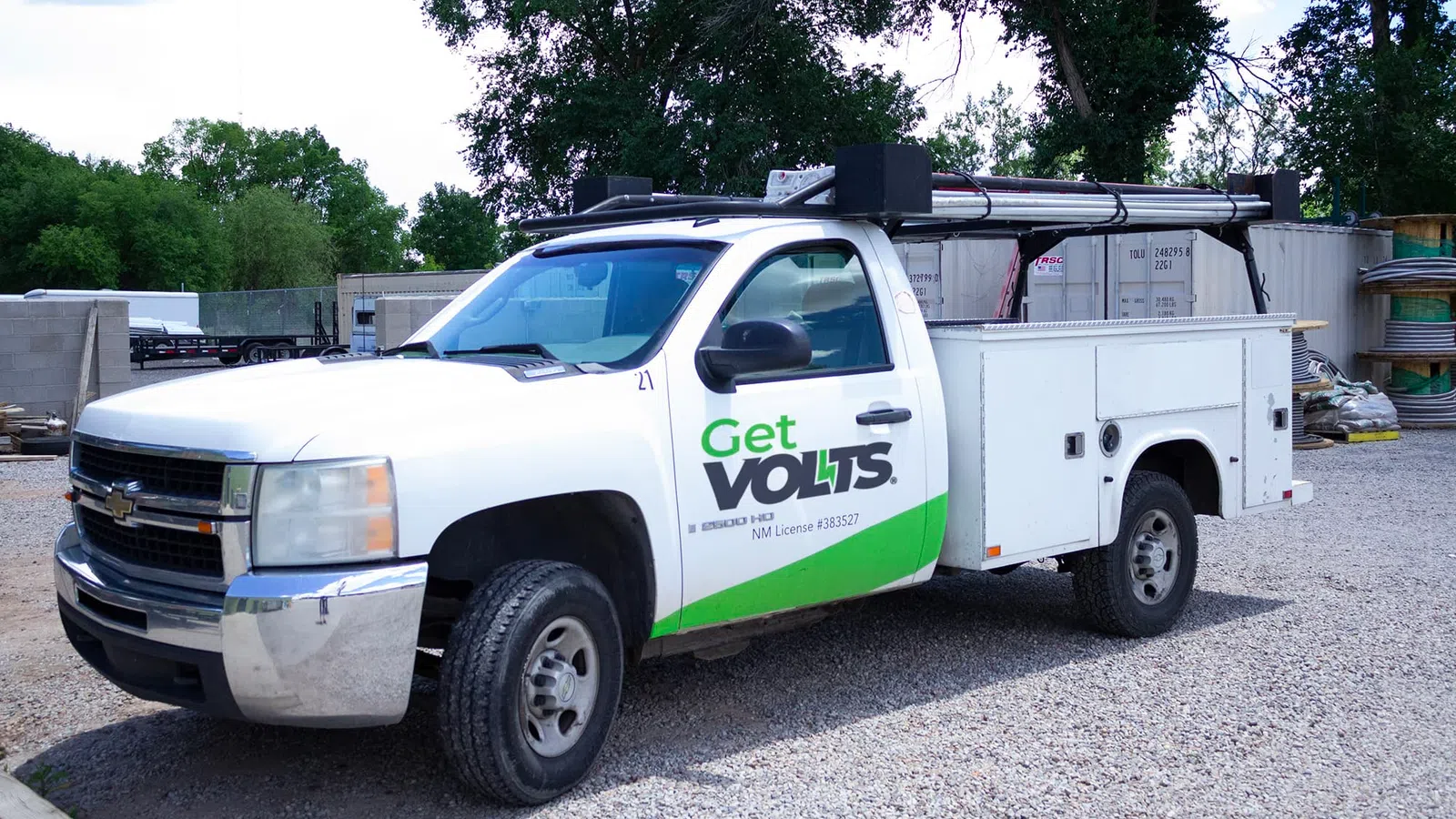 White utility truck with Get Volts logo parked on gravel in an industrial outdoor setting with trees in background