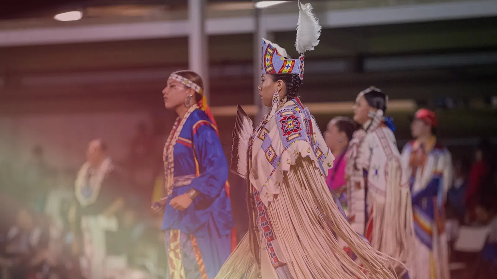Women dressed in colorful Native American regalia performing a traditional dance during a cultural event.