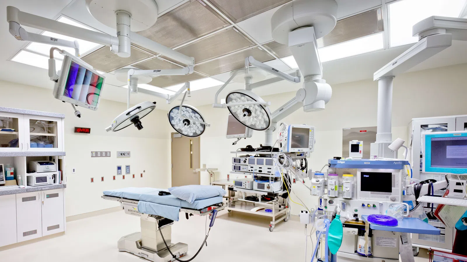 Modern hospital operating room with surgical lights, monitors, and medical equipment around the operating table.