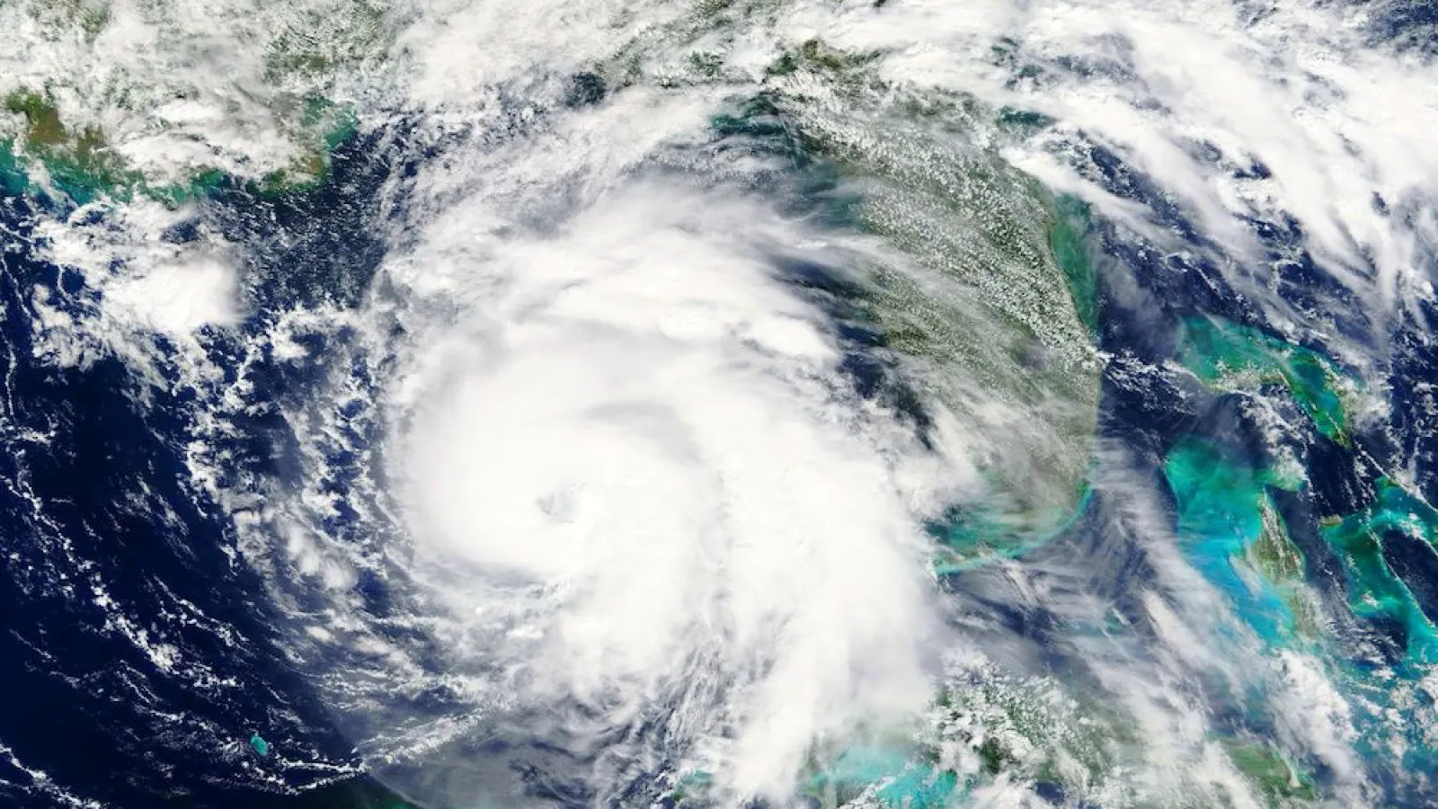 Satellite image of a swirling hurricane approaching a coastline with dense cloud formations and ocean visible.