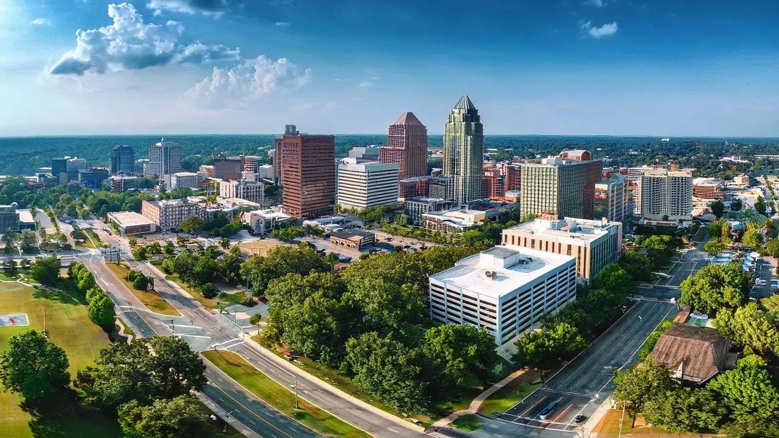 Nighttime cityscape of Raleigh, North Carolina with illuminated downtown buildings and light trails on the highway.