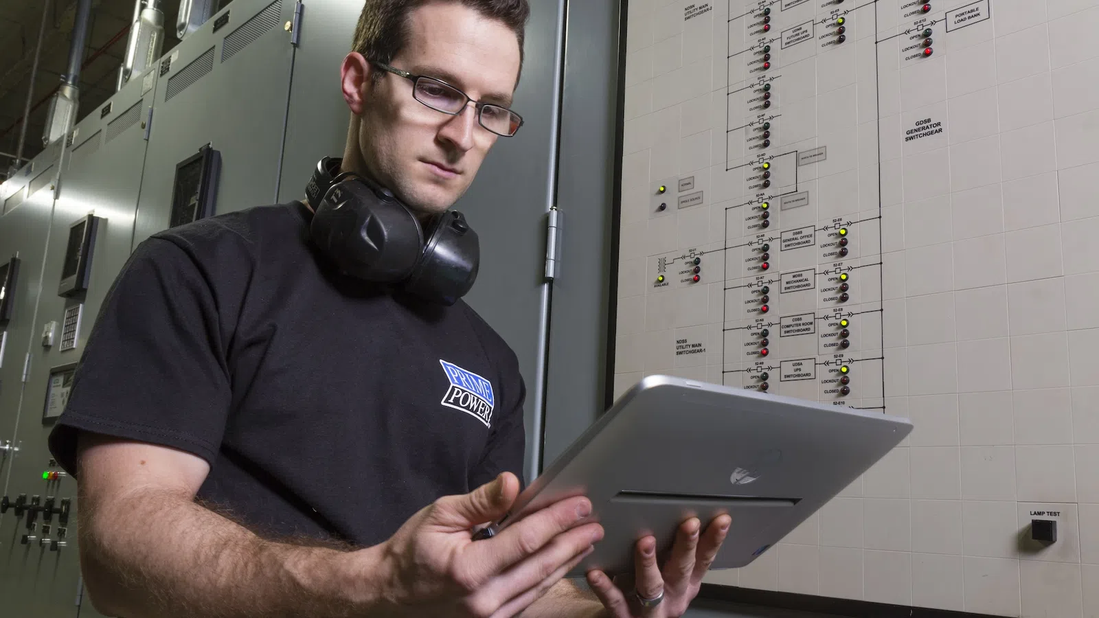 Technician in a control room using a tablet to monitor electrical systems and safety equipment.